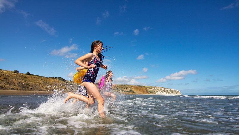 2 children running in to the sea at Yaverland. the sky is blue with a small scattering of clouds and there is a white cliff in the background